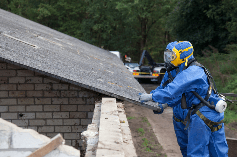 Workers in hazmat suits remove asbestos roofing.