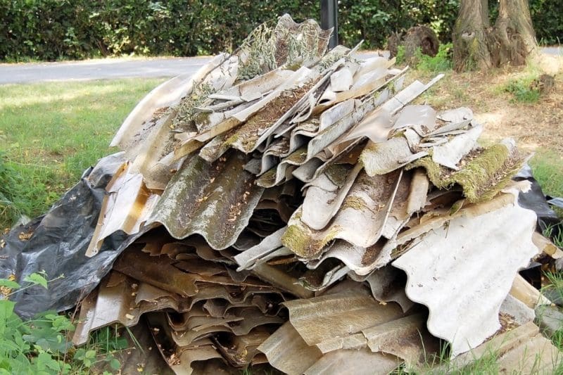 Stack of discarded corrugated roof panels on grass.