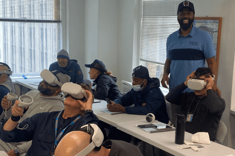 People using VR headsets in a classroom setting, overseen by an instructor.