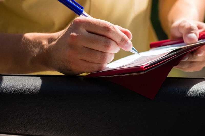 Person writing on clipboard, likely roadside inspection.