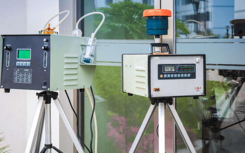 Outdoor air quality monitoring devices on tripods next to building.