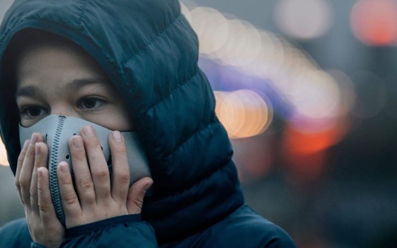 Child wearing a mask in a city with blurred lights in background.