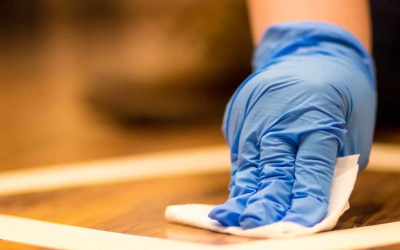 Cleaning a wooden surface with a gloved hand.