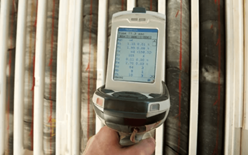 Hand holding a scanning device in front of stacked rock samples.