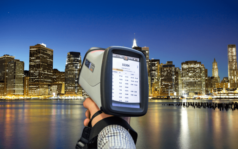 Handheld spectrometer analyzing material with city skyline in background.