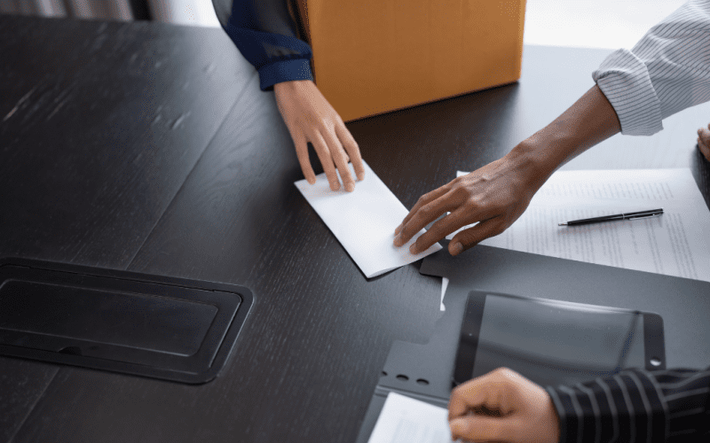 Hands exchanging an envelope over a desk with documents.