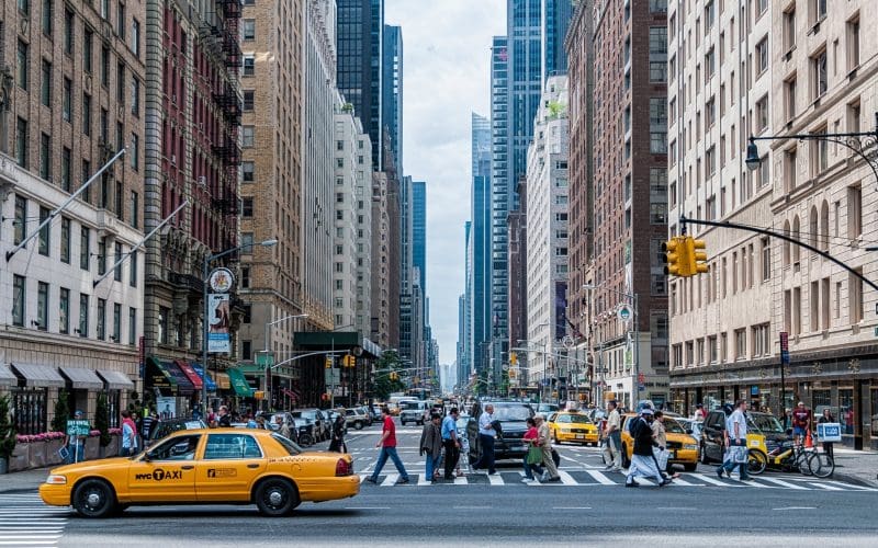 Busy New York City street with taxis and pedestrians crossing.