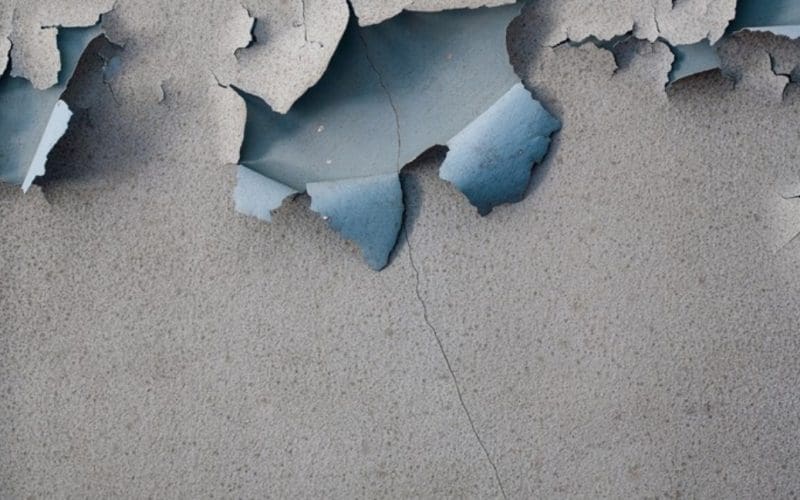 Cracked, peeling gray wall revealing blue paint beneath.