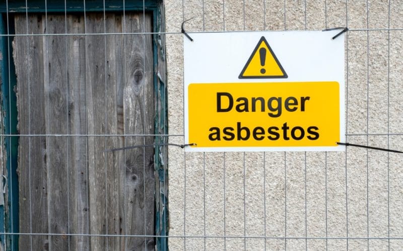 Warning sign for asbestos hazard on boarded window.