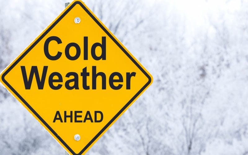 Warning sign for cold weather ahead with snowy background.
