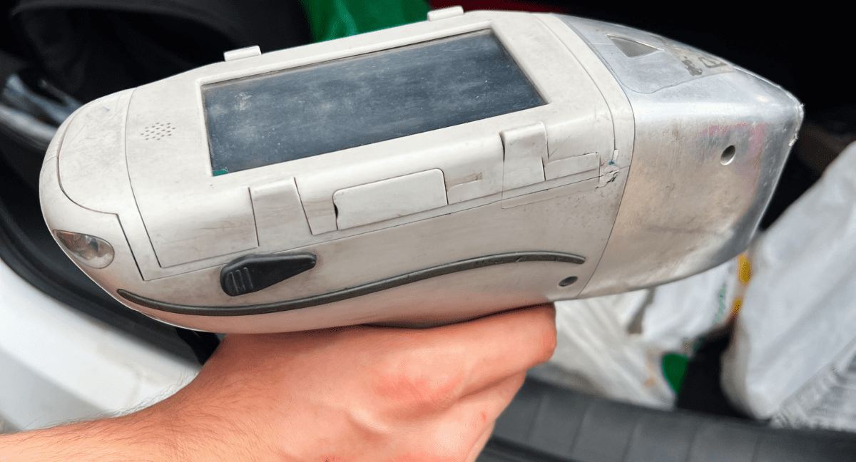 Hand holding a handheld scanner device in a vehicle.