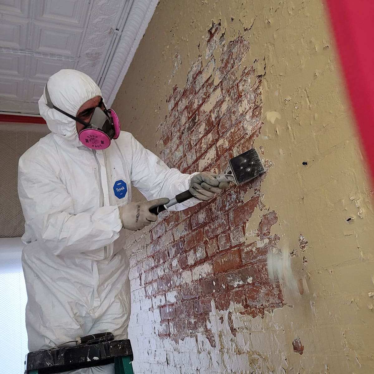 Worker removing wall paint in protective gear.