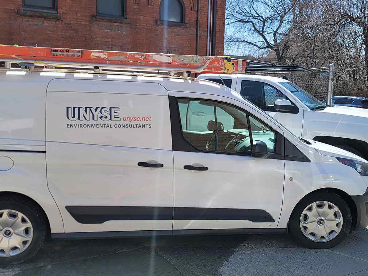 UNYSE environmental consultants van parked outside brick building.